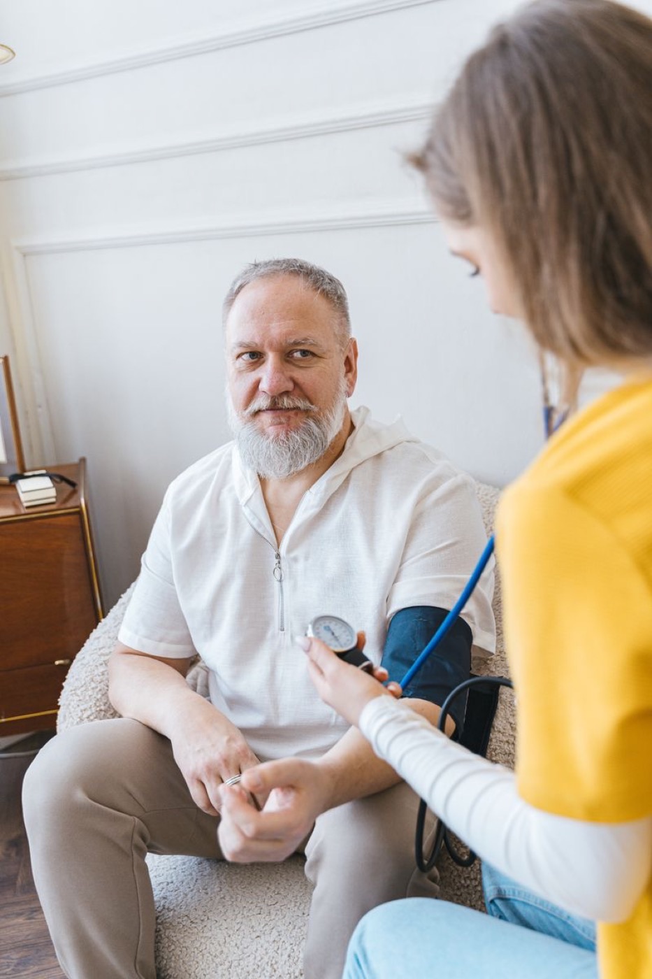 A clinician taking an older man’s blood pressure in his own front room, the two of them talking as she works.