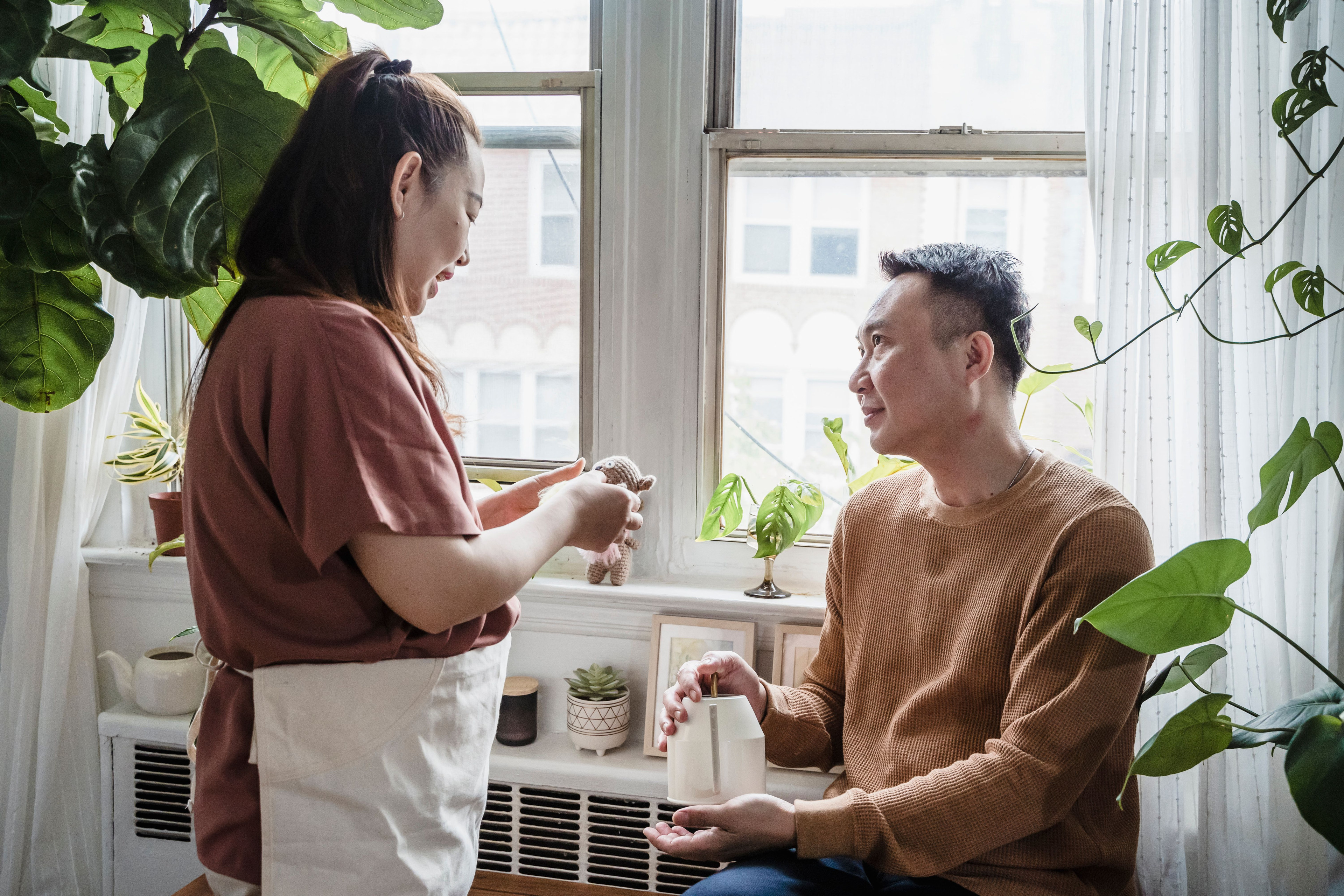 A couple in their fifties talking together by the window of their flat, in daylight.