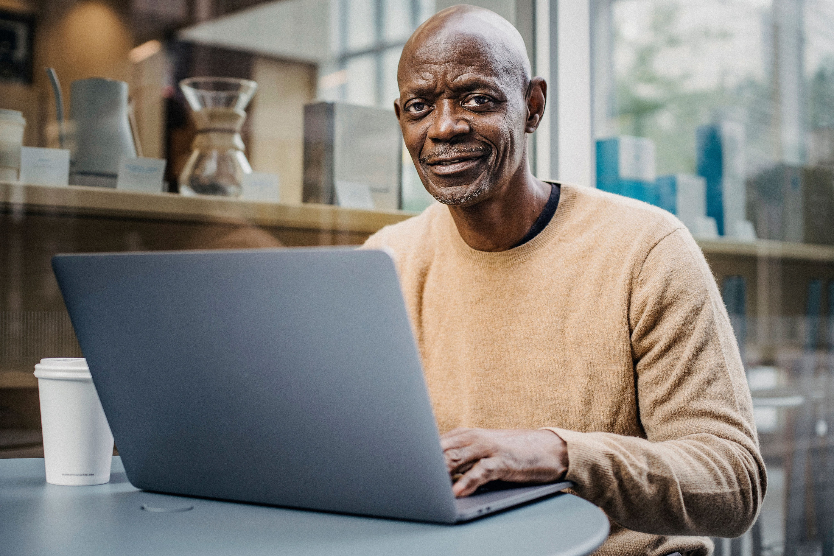 A man in his fifties at a laptop by a window at home.