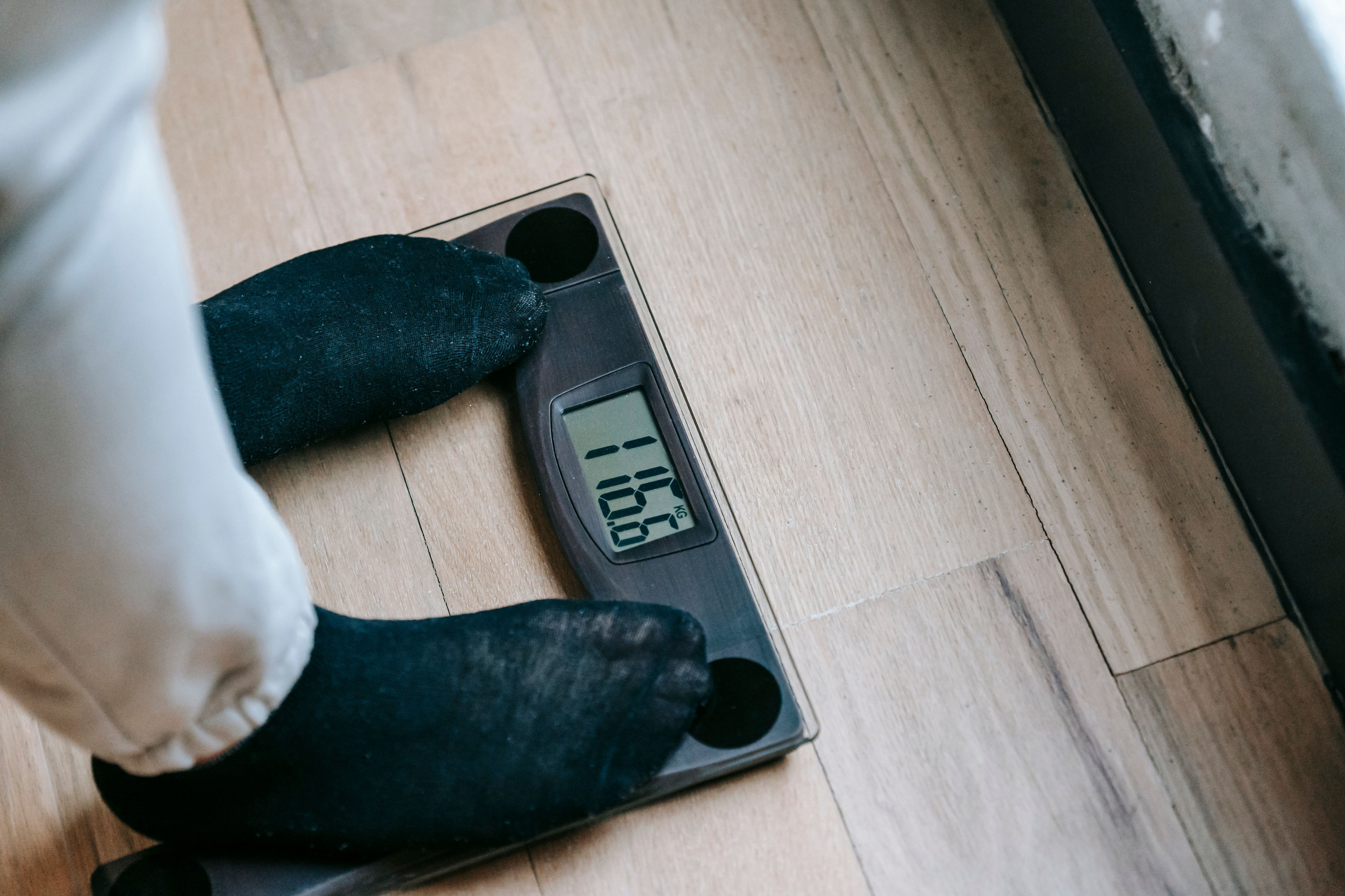 Feet in dark socks on a bathroom scale on a wooden floor, first thing in the morning.